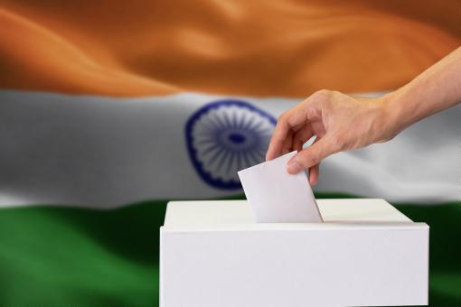 Close-up of human hand casting and inserting a vote in polling box with India flag blended in background