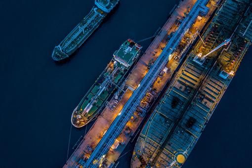 Aerial view Crude oil tanker under cargo operations on typical shore station with clearly visible mechanical loading arms and pipeline infrastructure.